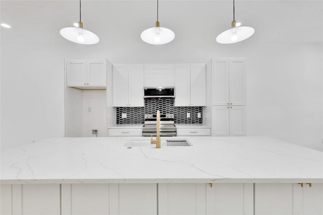 kitchen with appliances with stainless steel finishes, backsplash, light stone counters, pendant lighting, and white cabinets