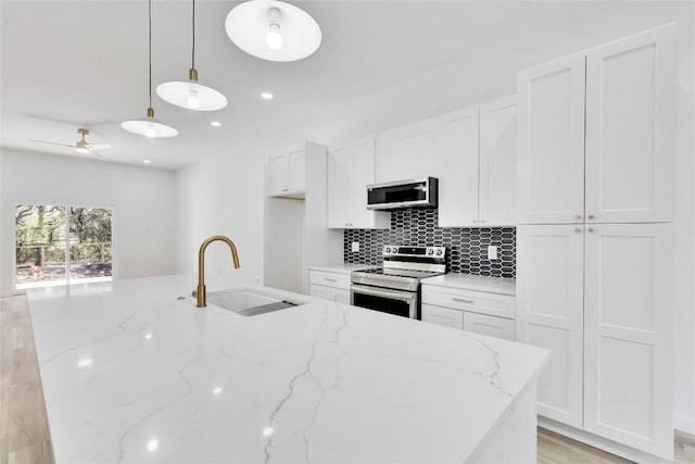 kitchen with sink, white cabinets, stainless steel appliances, and decorative light fixtures