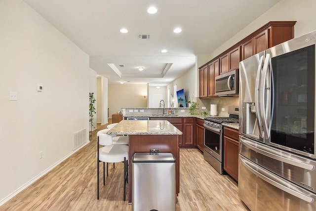 kitchen with stainless steel appliances, sink, a kitchen bar, kitchen peninsula, and a tray ceiling