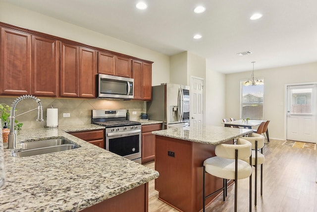 kitchen featuring light stone countertops, pendant lighting, stainless steel appliances, a notable chandelier, and sink