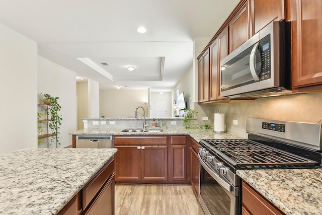 kitchen with stainless steel appliances, light wood-type flooring, light stone counters, a tray ceiling, and sink