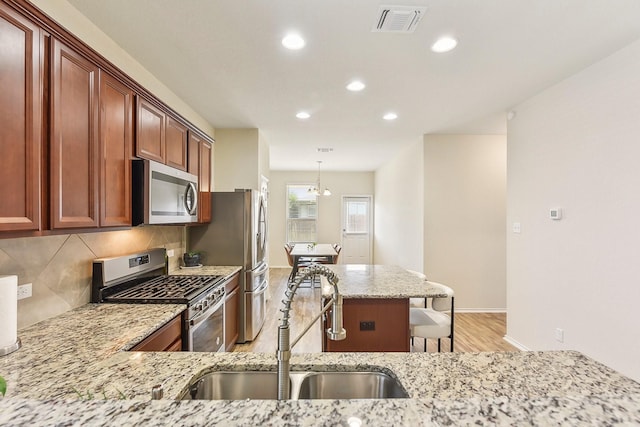 kitchen featuring stainless steel appliances, light stone counters, decorative backsplash, sink, and decorative light fixtures