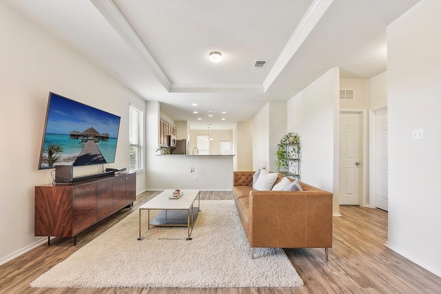 living room with light hardwood / wood-style floors, a tray ceiling, and crown molding