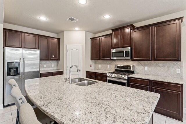 kitchen with light tile patterned flooring, tasteful backsplash, sink, a breakfast bar, and appliances with stainless steel finishes