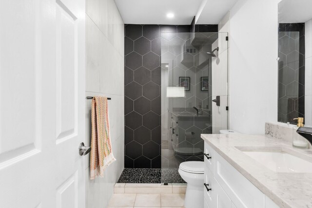 bathroom with toilet, tile walls, a tile shower, tile patterned floors, and vanity