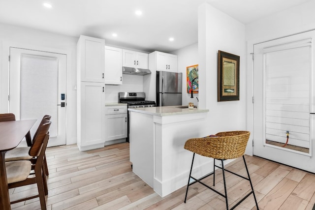 kitchen featuring stainless steel appliances, white cabinets, light hardwood / wood-style floors, a kitchen bar, and kitchen peninsula