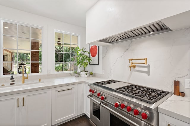 kitchen featuring white cabinets, backsplash, premium range hood, range with two ovens, and sink