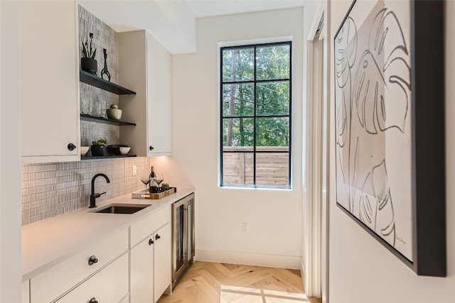 interior space with light parquet floors, sink, decorative backsplash, and white cabinetry