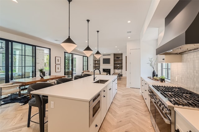 kitchen with custom range hood, an island with sink, stainless steel appliances, white cabinetry, and light parquet flooring