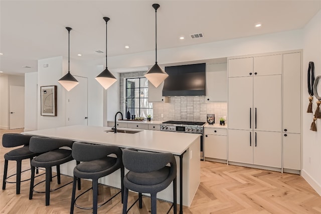 kitchen featuring light parquet flooring, an island with sink, sink, hanging light fixtures, and custom range hood