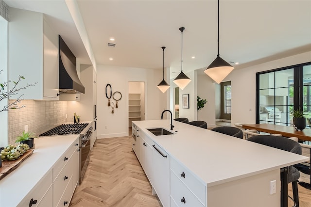 kitchen featuring white cabinetry, sink, wall chimney exhaust hood, an island with sink, and pendant lighting