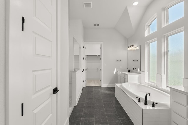 bathroom featuring tile patterned floors, a relaxing tiled tub, a healthy amount of sunlight, and vaulted ceiling