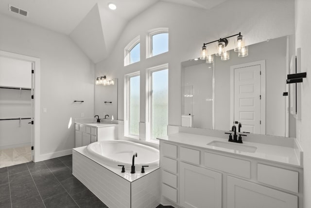 bathroom with tile patterned flooring, vanity, lofted ceiling, and tiled tub