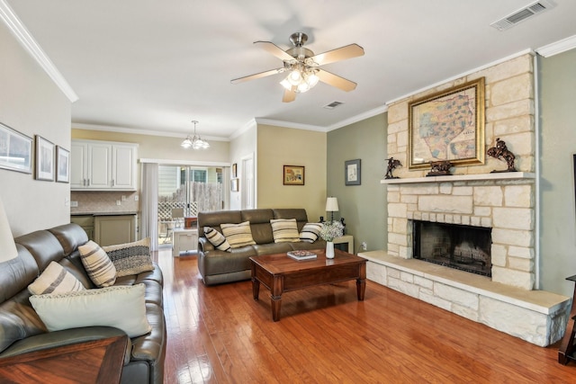 living room with crown molding, a fireplace, ceiling fan with notable chandelier, and hardwood / wood-style flooring