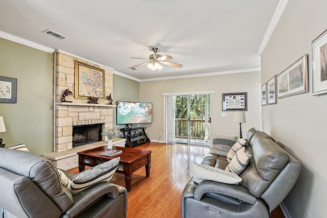 living room featuring a stone fireplace, ceiling fan, light hardwood / wood-style floors, and ornamental molding