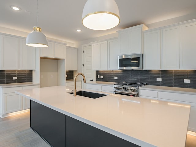 kitchen featuring appliances with stainless steel finishes, hanging light fixtures, sink, an island with sink, and white cabinets