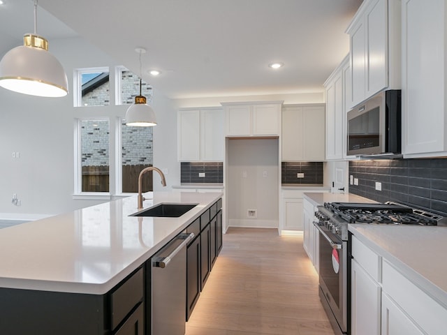 kitchen with stainless steel appliances, a kitchen island with sink, white cabinetry, and decorative light fixtures