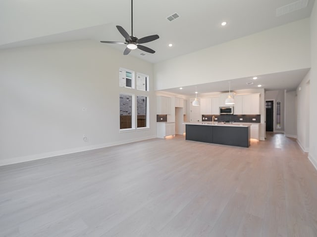 unfurnished living room featuring high vaulted ceiling, light hardwood / wood-style flooring, ceiling fan, and sink