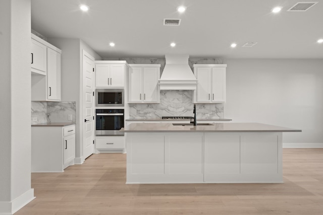 kitchen with premium range hood, stainless steel appliances, white cabinetry, and a center island with sink