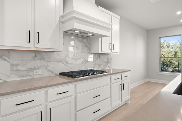 kitchen with premium range hood, backsplash, white cabinets, and stainless steel gas stovetop