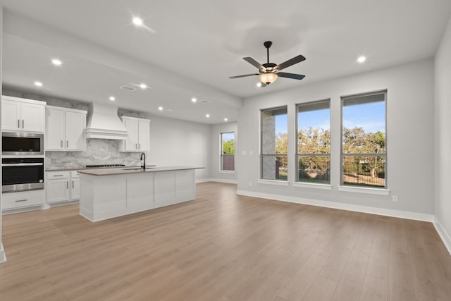 kitchen featuring premium range hood, white cabinets, a kitchen island with sink, decorative backsplash, and stainless steel appliances