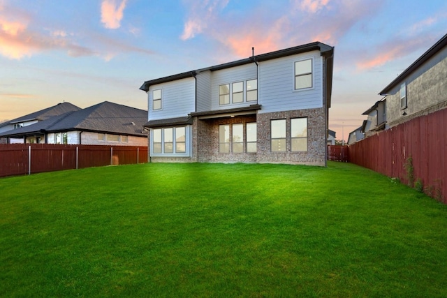 back house at dusk featuring a lawn