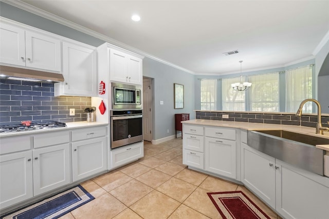 kitchen with appliances with stainless steel finishes, ornamental molding, sink, light tile patterned floors, and white cabinetry