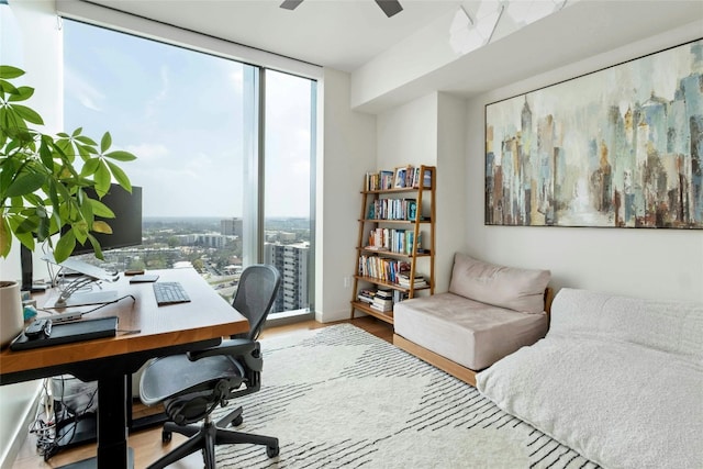 office area featuring expansive windows, wood-type flooring, a healthy amount of sunlight, and ceiling fan