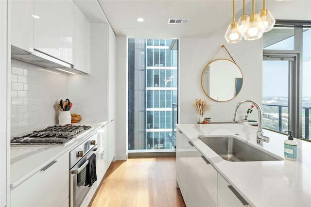 kitchen featuring pendant lighting, sink, white cabinets, stainless steel appliances, and light hardwood / wood-style flooring