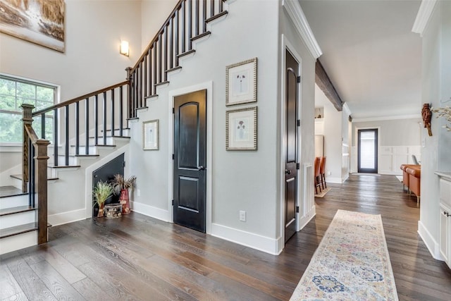 entrance foyer with dark wood-type flooring, ornamental molding, and a high ceiling