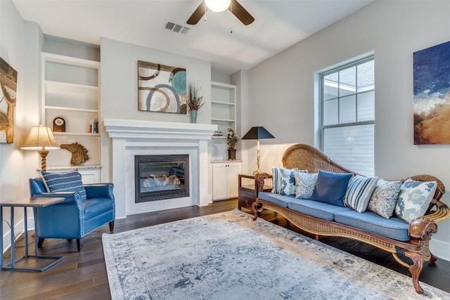 living room with built in shelves, dark hardwood / wood-style floors, and ceiling fan