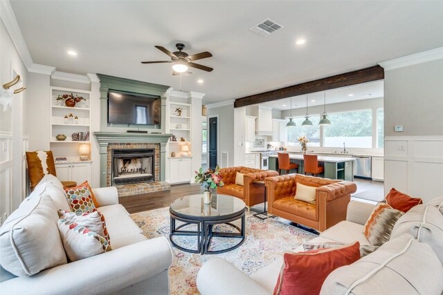 living room with a brick fireplace, ornamental molding, light wood-type flooring, and ceiling fan