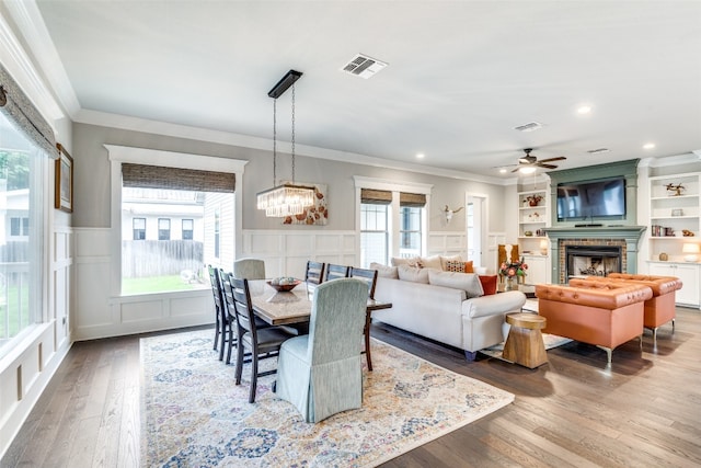 dining space with crown molding, hardwood / wood-style flooring, ceiling fan with notable chandelier, and built in features