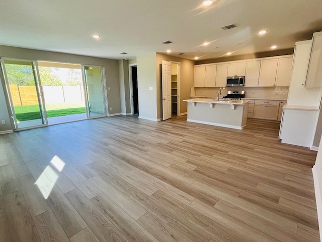 kitchen with a kitchen bar, stainless steel appliances, a center island with sink, white cabinetry, and light hardwood / wood-style flooring