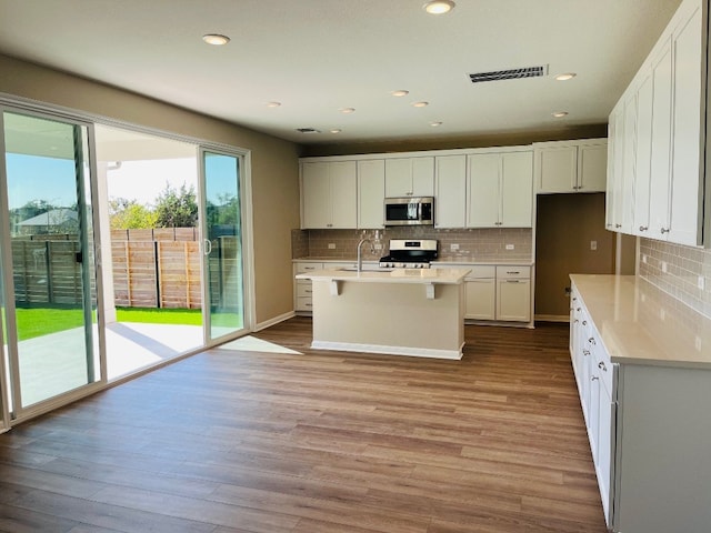 kitchen featuring stainless steel appliances, white cabinets, an island with sink, and light wood-type flooring