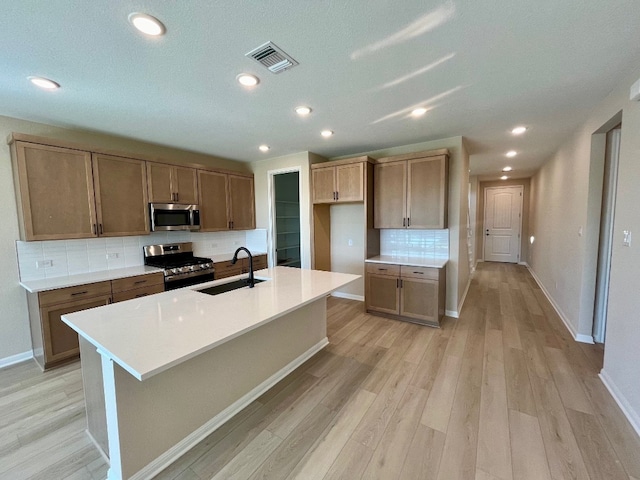 kitchen featuring decorative backsplash, appliances with stainless steel finishes, sink, light hardwood / wood-style flooring, and an island with sink