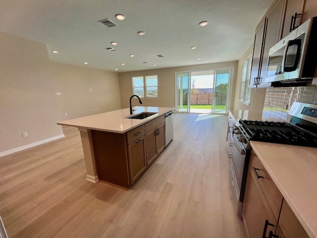 kitchen with tasteful backsplash, stainless steel appliances, a kitchen island with sink, sink, and light hardwood / wood-style floors