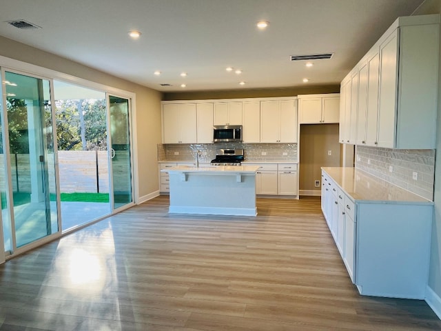 kitchen with light hardwood / wood-style floors, a center island with sink, appliances with stainless steel finishes, white cabinets, and decorative backsplash