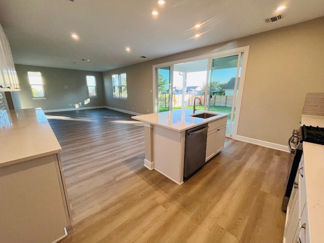 kitchen with white cabinets, light hardwood / wood-style floors, a center island with sink, and dishwasher