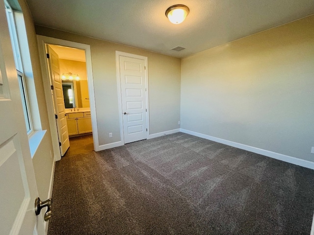 unfurnished bedroom featuring dark colored carpet, a closet, and connected bathroom