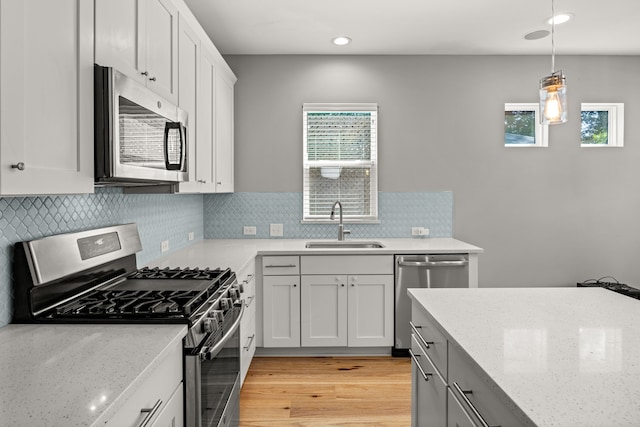 kitchen with light stone counters, decorative light fixtures, white cabinetry, appliances with stainless steel finishes, and sink