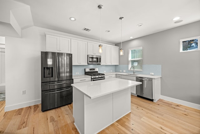 kitchen with appliances with stainless steel finishes, a kitchen island, white cabinets, decorative light fixtures, and sink