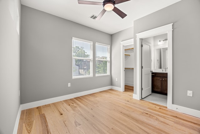 unfurnished bedroom featuring ensuite bathroom, ceiling fan, light hardwood / wood-style flooring, a closet, and a walk in closet