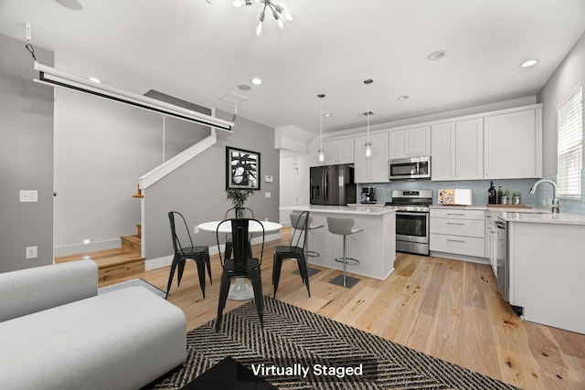 kitchen with a center island, hanging light fixtures, stainless steel appliances, white cabinetry, and sink