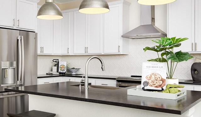 kitchen with tasteful backsplash, stainless steel appliances, wall chimney range hood, decorative light fixtures, and white cabinets