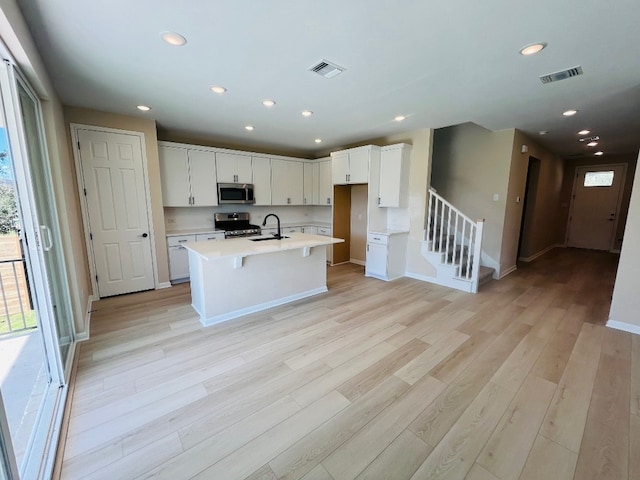 kitchen with sink, appliances with stainless steel finishes, an island with sink, light hardwood / wood-style flooring, and white cabinets