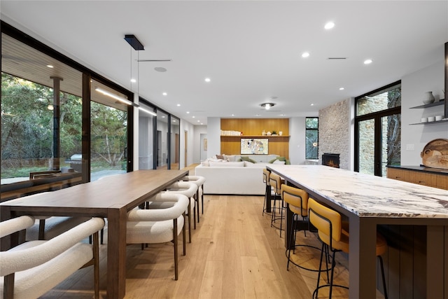 dining area featuring a stone fireplace, expansive windows, light hardwood / wood-style flooring, and a healthy amount of sunlight