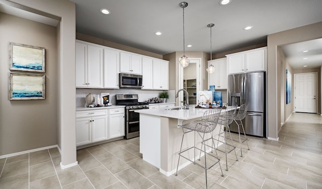 kitchen with stainless steel appliances, tasteful backsplash, pendant lighting, a center island with sink, and white cabinets