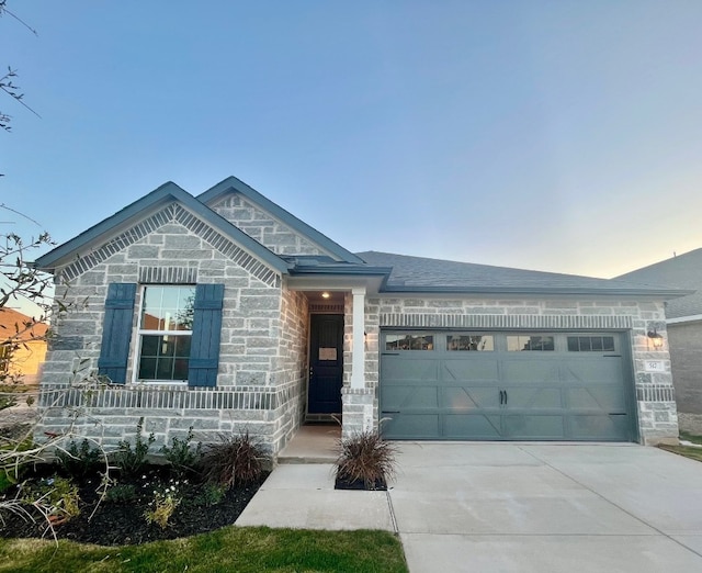 view of front of property featuring a garage, concrete driveway, a shingled roof, and stone siding