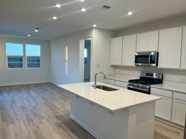 kitchen featuring a kitchen island with sink, sink, light wood-type flooring, white cabinetry, and stainless steel appliances